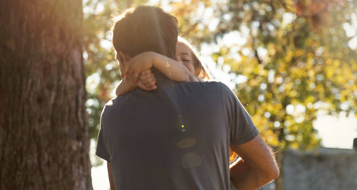 Ein Vater trägt sein Kind liebevoll im Arm und umarmt es sanft, während sie einen Moment der Nähe und Geborgenheit teilen – ein Zeichen der unendlichen Liebe und Verbundenheit Vater und Kind