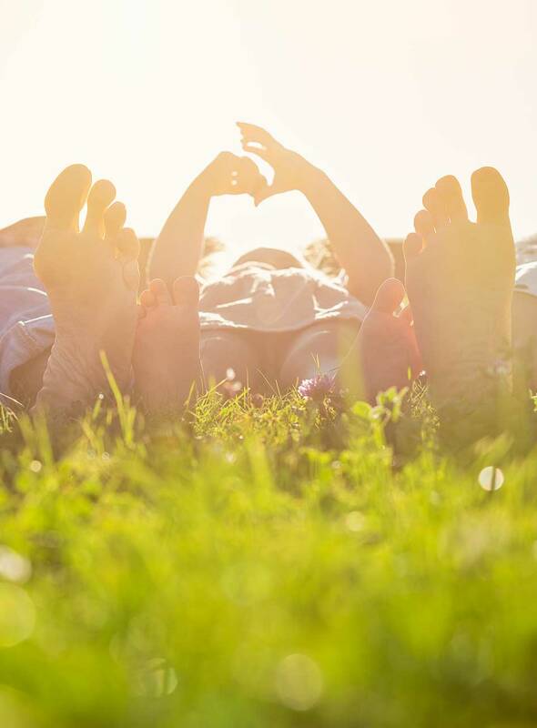 Eine Familie liegt entspannt gemeinsam im Gras, genießt die Sonne und die frische Luft, während das Kind neugierig die Umgebung erkundet – ein Moment der Ruhe und Verbundenheit in der Natur Familie im Gras