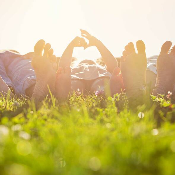 Eine Familie liegt entspannt gemeinsam im Gras, genießt die Sonne und die frische Luft, während das Kind neugierig die Umgebung erkundet – ein Moment der Ruhe und Verbundenheit in der Natur Familie im Gras
